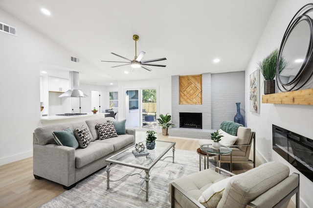 living room featuring ceiling fan, lofted ceiling, a fireplace, and light hardwood / wood-style flooring