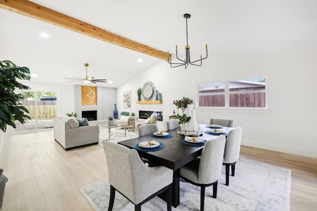 dining area with lofted ceiling with beams, light wood-type flooring, a large fireplace, and ceiling fan with notable chandelier