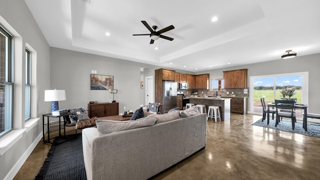 living room with ceiling fan, a raised ceiling, and sink