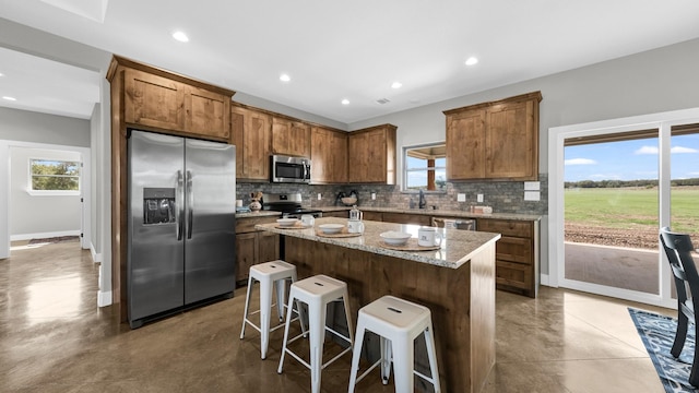 kitchen with a center island, decorative backsplash, appliances with stainless steel finishes, a breakfast bar area, and light stone counters