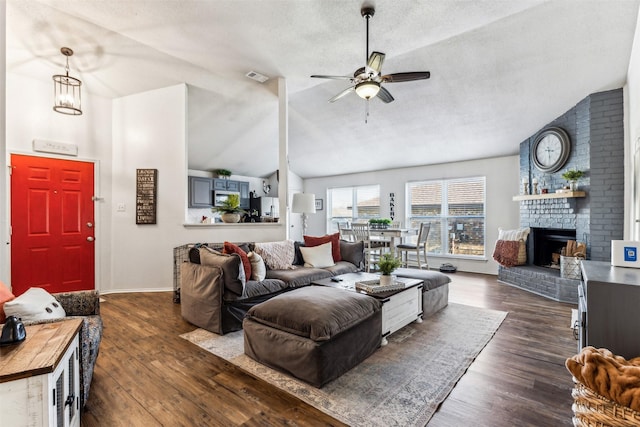 living room featuring lofted ceiling, a fireplace, dark hardwood / wood-style flooring, and ceiling fan with notable chandelier