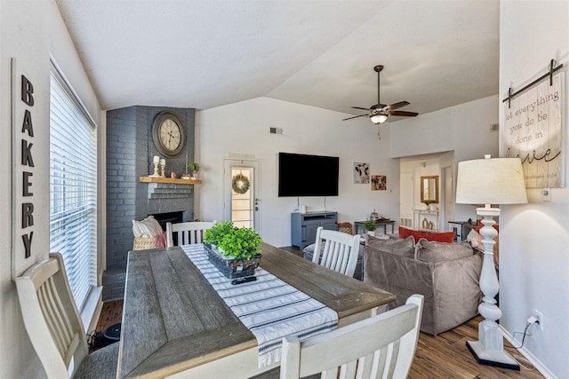 dining area with ceiling fan, vaulted ceiling, a brick fireplace, and hardwood / wood-style flooring