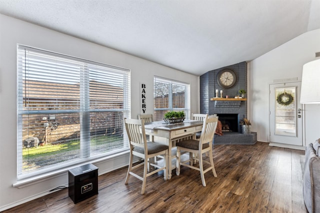 dining area with dark wood-type flooring, vaulted ceiling, a fireplace, and a textured ceiling