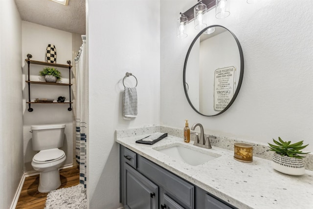 bathroom with wood-type flooring, toilet, vanity, and a textured ceiling