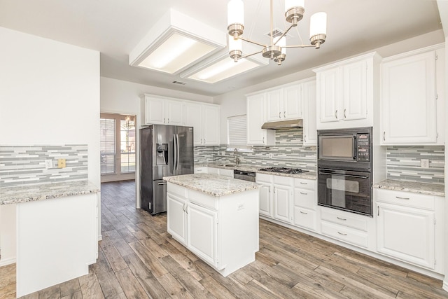 kitchen with a kitchen island, black appliances, white cabinetry, hanging light fixtures, and light stone counters