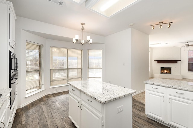 kitchen with dark wood-type flooring, hanging light fixtures, light stone countertops, a kitchen island, and white cabinets