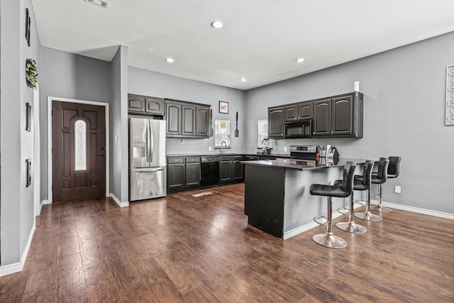 kitchen with black appliances, a kitchen bar, sink, dark hardwood / wood-style floors, and kitchen peninsula