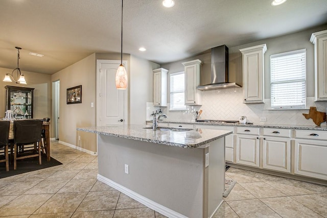 kitchen featuring an island with sink, white cabinets, wall chimney exhaust hood, and sink