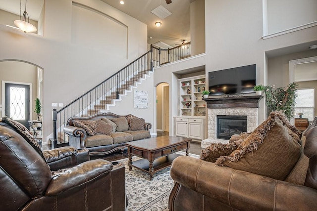 living room featuring ceiling fan, built in shelves, a fireplace, and a towering ceiling