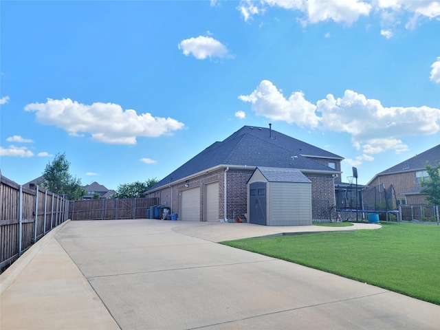 view of side of property featuring a trampoline, a garage, a storage unit, and a yard