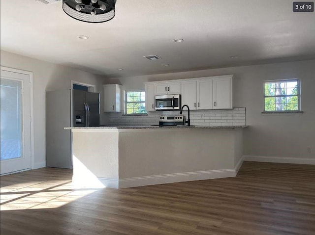 kitchen with kitchen peninsula, stainless steel appliances, dark hardwood / wood-style floors, stone counters, and white cabinets