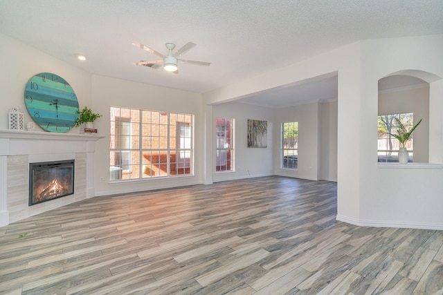 unfurnished living room with ceiling fan, a tile fireplace, a textured ceiling, and light hardwood / wood-style floors