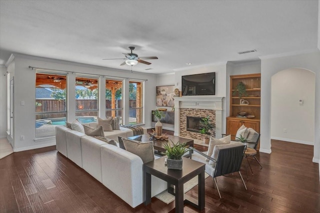 living room featuring ceiling fan, dark hardwood / wood-style floors, crown molding, and a fireplace