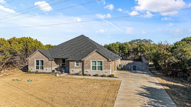 view of front facade with stone siding, fence, roof with shingles, concrete driveway, and brick siding