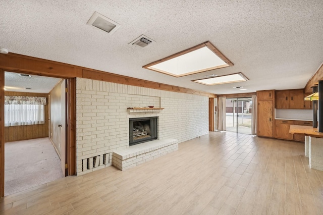 unfurnished living room featuring a brick fireplace, light hardwood / wood-style floors, a skylight, and wooden walls