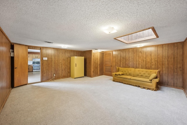 unfurnished room with a textured ceiling, light colored carpet, and wood walls