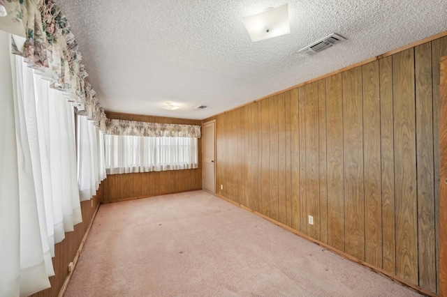 carpeted spare room with a textured ceiling and wood walls