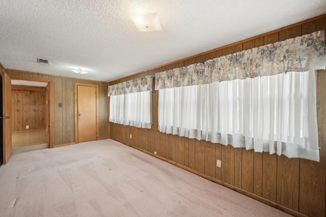 carpeted spare room with a textured ceiling and wood walls