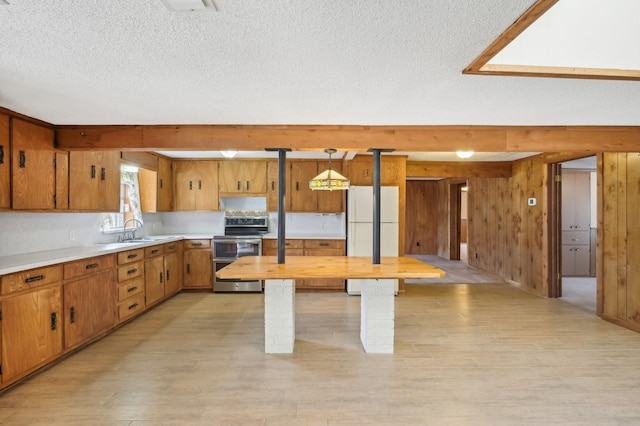 kitchen featuring white fridge, double oven range, hanging light fixtures, sink, and wood walls