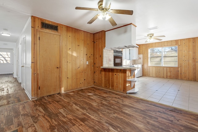 unfurnished living room featuring ceiling fan, plenty of natural light, wooden walls, and dark hardwood / wood-style floors