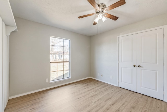 unfurnished bedroom featuring ceiling fan, a closet, light hardwood / wood-style flooring, and multiple windows