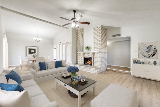 living room featuring a brick fireplace, light hardwood / wood-style floors, lofted ceiling with beams, a textured ceiling, and ceiling fan with notable chandelier