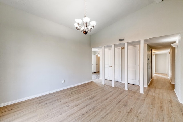 spare room featuring high vaulted ceiling, light hardwood / wood-style flooring, and an inviting chandelier