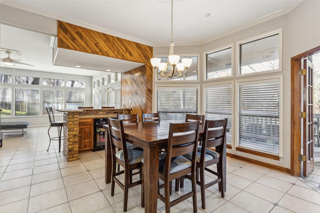 tiled dining room featuring ornamental molding, ceiling fan with notable chandelier, beverage cooler, and wooden walls