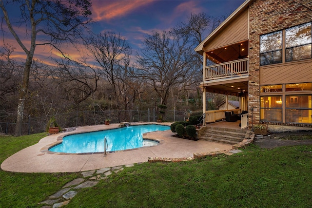 pool at dusk with a patio area and a lawn