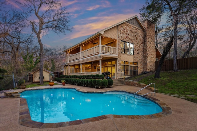 pool at dusk with ceiling fan and a storage shed