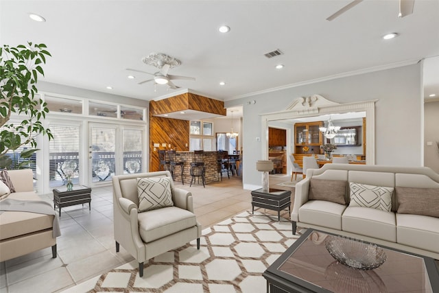 living room featuring light tile patterned floors, crown molding, ceiling fan with notable chandelier, and wood walls