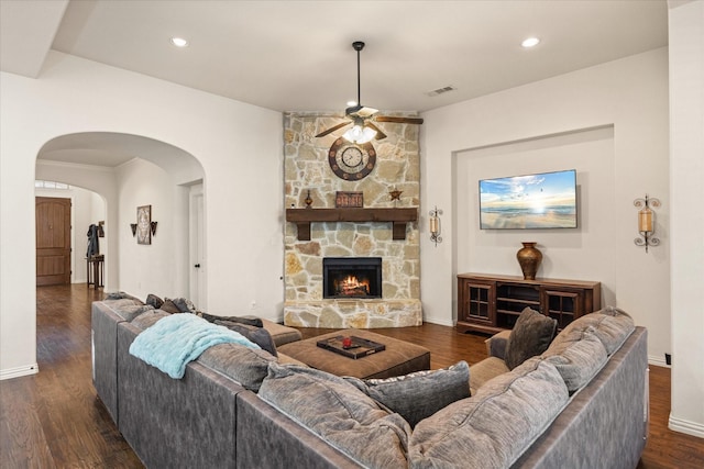 living room with dark wood-type flooring, a stone fireplace, and ceiling fan