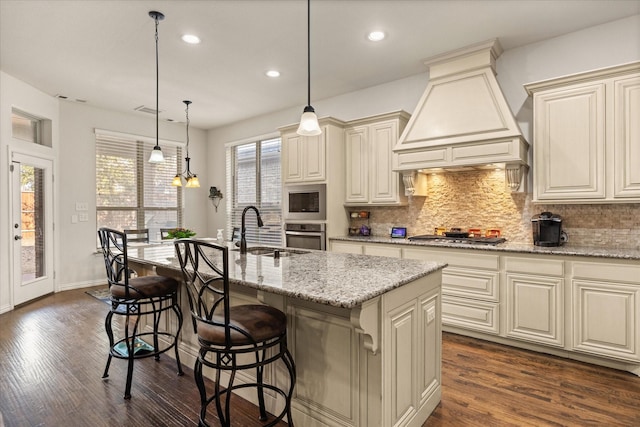 kitchen with premium range hood, a center island with sink, appliances with stainless steel finishes, decorative light fixtures, and sink