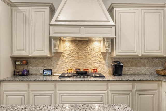 kitchen with stainless steel gas stovetop, tasteful backsplash, light stone counters, and custom range hood