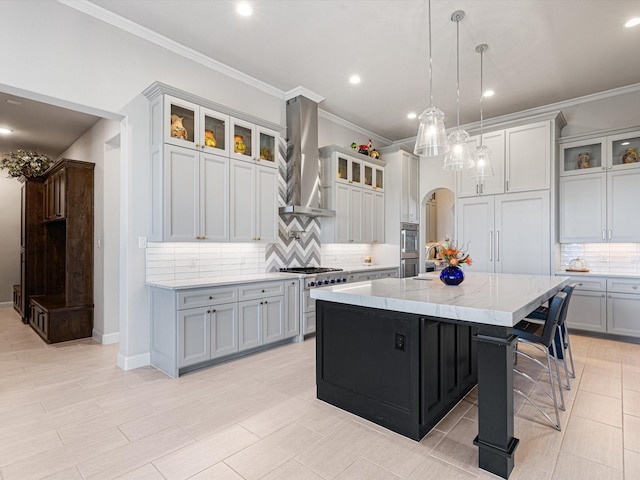 kitchen featuring an island with sink, stainless steel appliances, hanging light fixtures, light stone countertops, and wall chimney exhaust hood