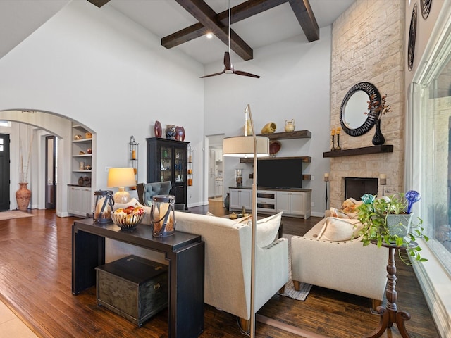 living room featuring dark hardwood / wood-style flooring, beamed ceiling, a fireplace, built in features, and ceiling fan