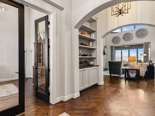 hallway featuring built in shelves, french doors, dark parquet flooring, and a chandelier