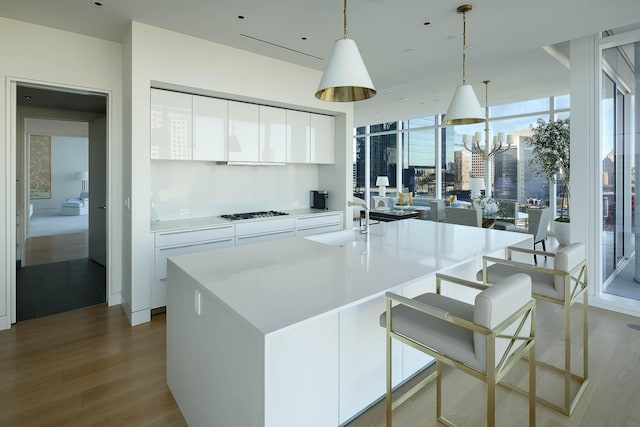 kitchen featuring white cabinets, sink, hanging light fixtures, a kitchen island with sink, and light wood-type flooring