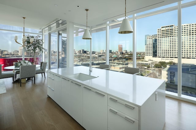 kitchen featuring pendant lighting, white cabinets, expansive windows, and an island with sink