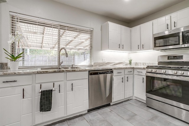 kitchen featuring stainless steel appliances, white cabinetry, light stone counters, and sink