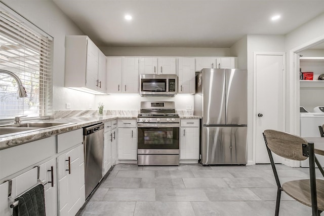 kitchen with washer and dryer, white cabinets, appliances with stainless steel finishes, and sink