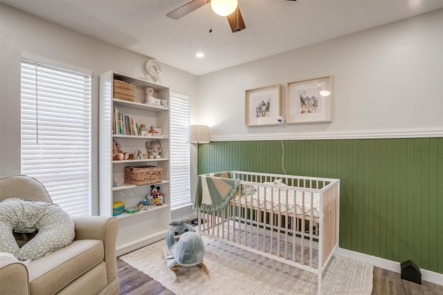 bedroom with ceiling fan, hardwood / wood-style floors, wooden walls, and a crib