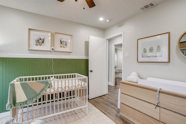 bedroom with ceiling fan, hardwood / wood-style floors, a nursery area, and wood walls