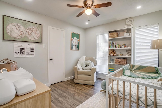 bedroom with ceiling fan, wood-type flooring, and a nursery area