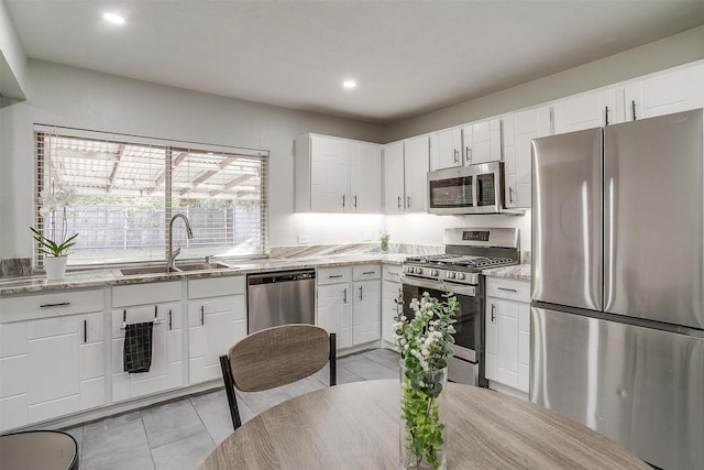 kitchen with appliances with stainless steel finishes, white cabinets, light stone counters, and sink