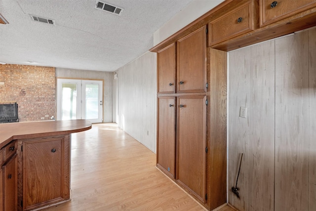 kitchen featuring a textured ceiling, a brick fireplace, light hardwood / wood-style flooring, and french doors