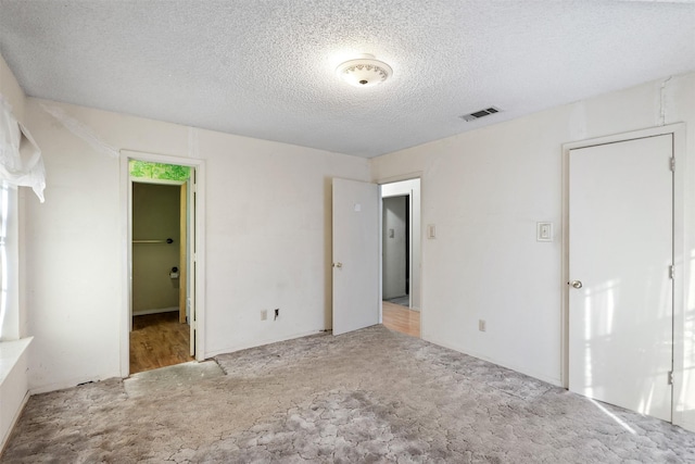 unfurnished bedroom featuring a textured ceiling, light carpet, a closet, and a walk in closet