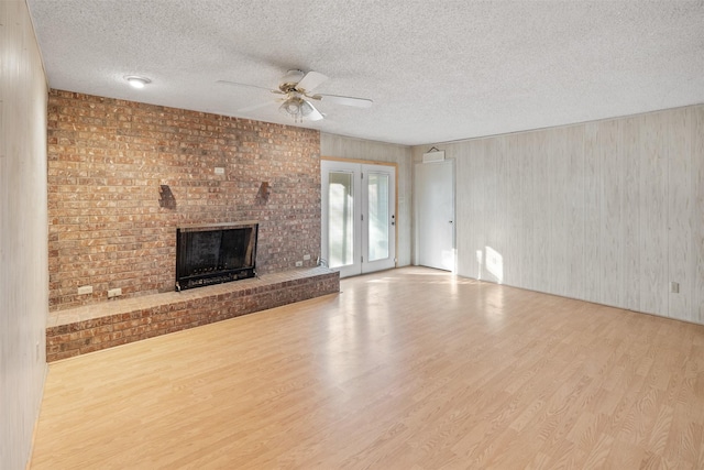 unfurnished living room featuring ceiling fan, a fireplace, light hardwood / wood-style floors, a textured ceiling, and french doors