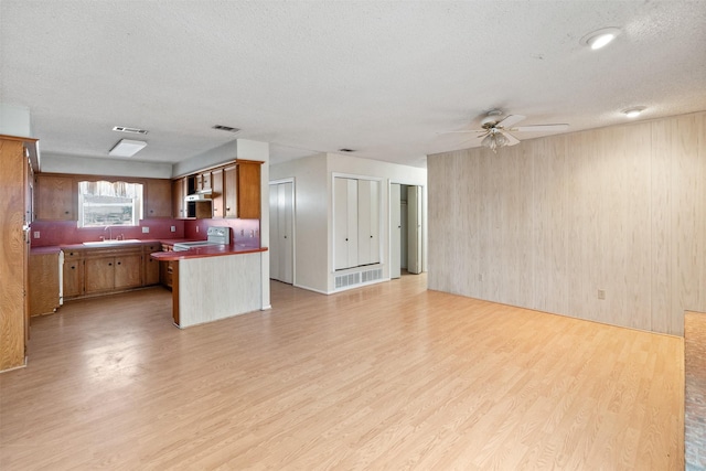 kitchen with ceiling fan, wooden walls, range with electric stovetop, light wood-type flooring, and a textured ceiling