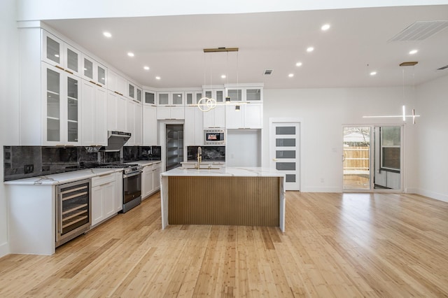 kitchen featuring pendant lighting, beverage cooler, white cabinets, and an island with sink